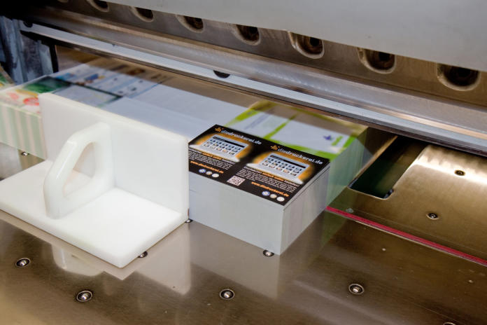 Een stapel kleurrijk bedrukte kaarten wordt in een drukkerij gesneden door een industriële papiersnijmachine.