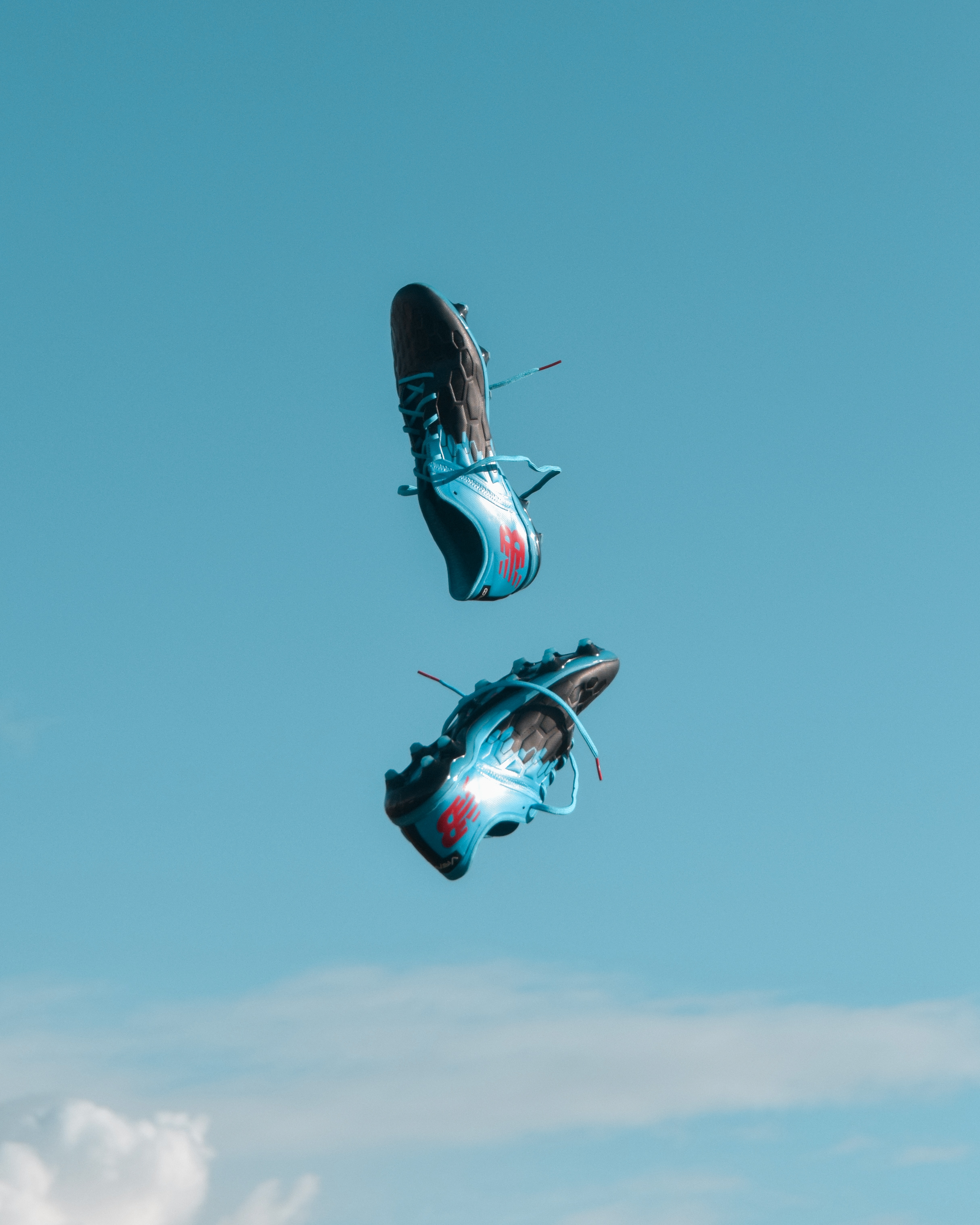 Twee blauw-zwarte voetbalschoenen, die doen denken aan de spanning rond het EM 2021 Spielplan, hangen in de lucht tegen een strakblauwe lucht met hier en daar wat wolken zichtbaar.