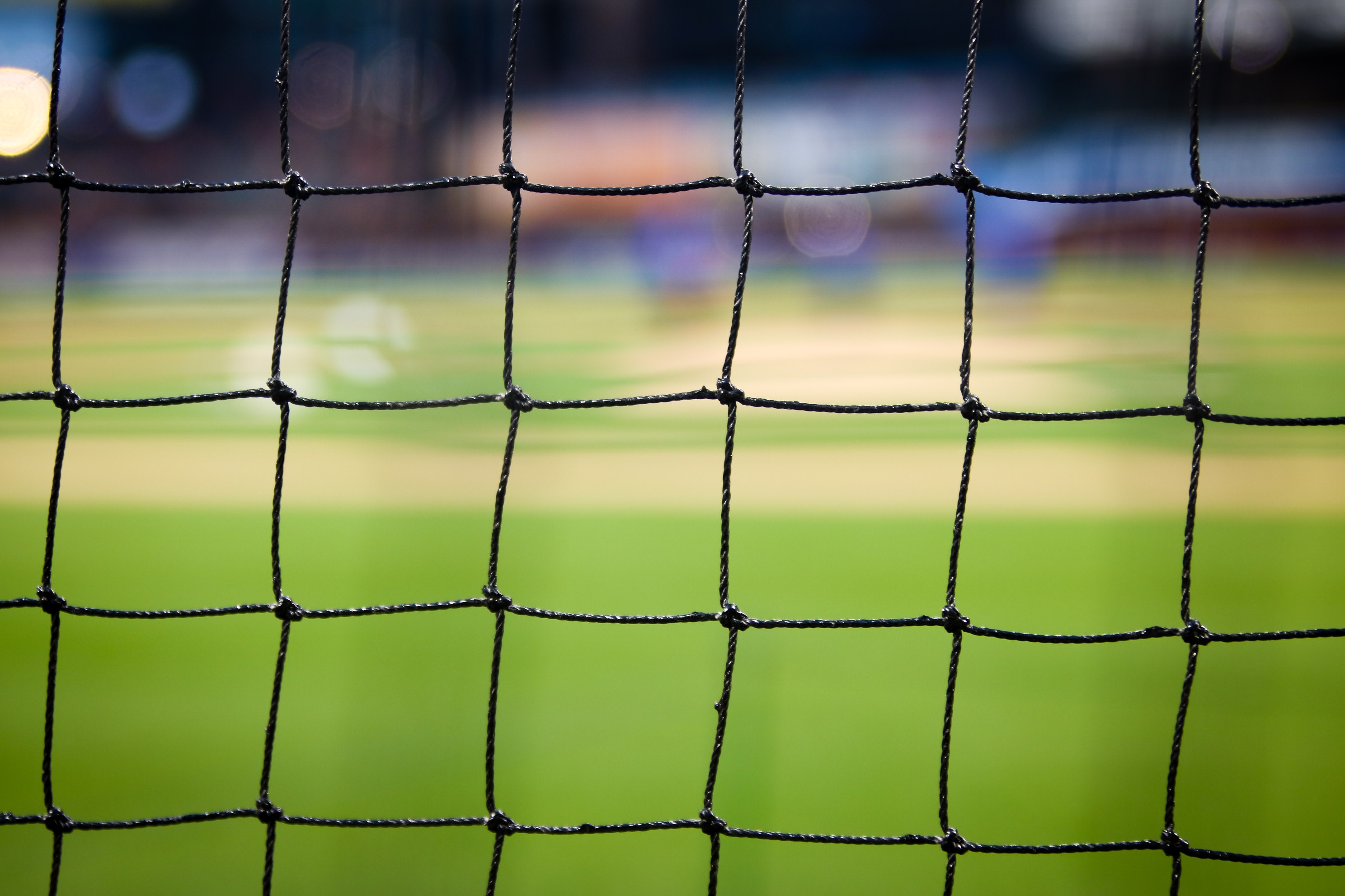 Close-up van een zwart net met een wazige achtergrond waarop een groen sportveld te zien is, mogelijk afkomstig uit het em 2021 spielplan. Het net is scherp in beeld, waardoor vierkante segmenten ontstaan die opvallen, terwijl het veld zelf prachtig onscherp blijft.