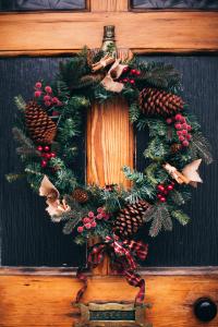 Een feestelijke kerstkrans op een houten deur, versierd met dennenappels, rode bessen en kleine kaneelstokjes. Er hangt een geruit lint onder voor een gezellige, feestelijke sfeer. Onder de krans is een messing brievenbus met het opschrift LETTERS zichtbaar.
