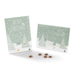 Twee adventskalenders met een besneeuwde kerstboom en de tekst Merry Christmas op een lichtgroene achtergrond. Verschillende kleine, chocoladeachtige stukjes liggen verspreid vooraan de kalenders.